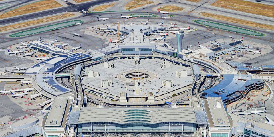 Aerial view of San Francisco International Airport: the international terminal, concourses, aprons with parked aircraft, the control tower, and construction on the airfield edge.